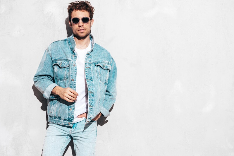 portrait-handsome-confident-stylish-hipster-lambersexual-model-with-curly-hairstyle-sexy-man-dressed-jeans-jacket-fashion male isolated grey wall studio sunglasses